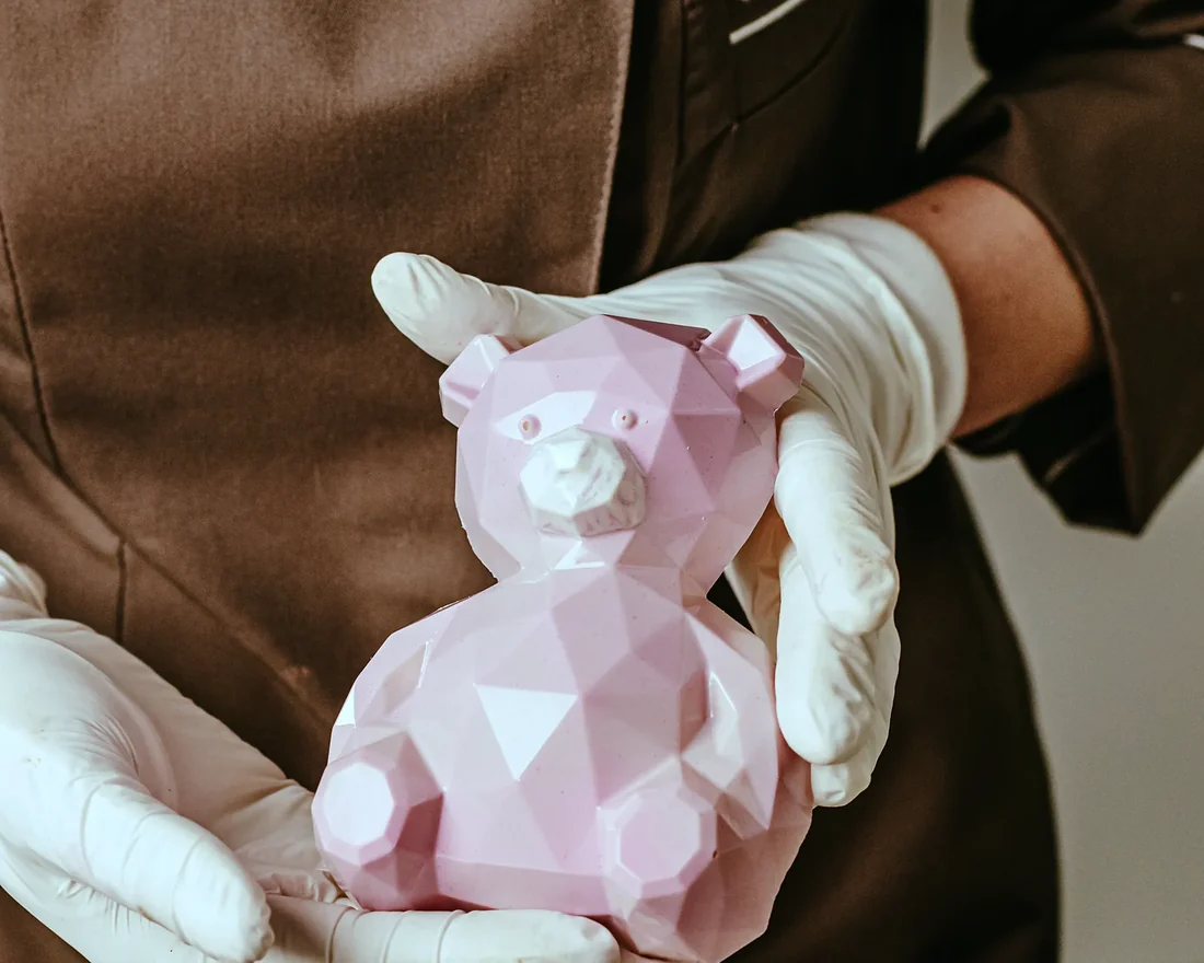 A faceted pink chocolate bear held in gloved hands
